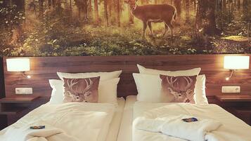 A hotel room with two beds, each with a deer-themed pillow, a nightstand with a lamp, and a forest mural on the wall.