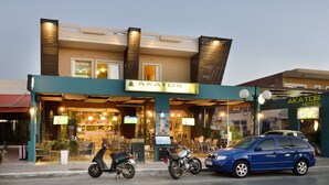 Un hotel con fachada moderna, mesas al aire libre y un área de restaurante visible.