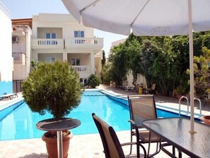 A pool area with a table and chairs, surrounded by potted plants and a building in the background. - Akatos Hotel (Chania)