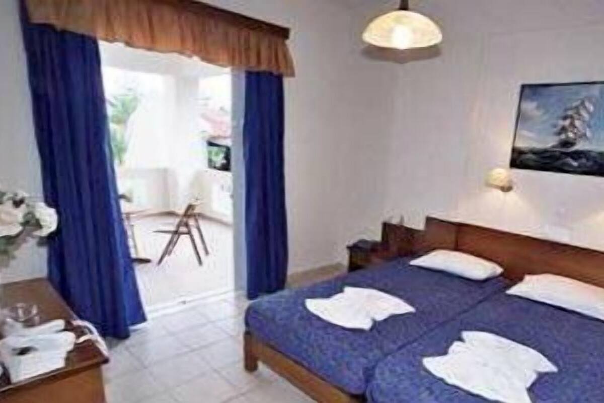 A hotel room with a bed, two bedside tables, a painting on the wall, and a view through the window.