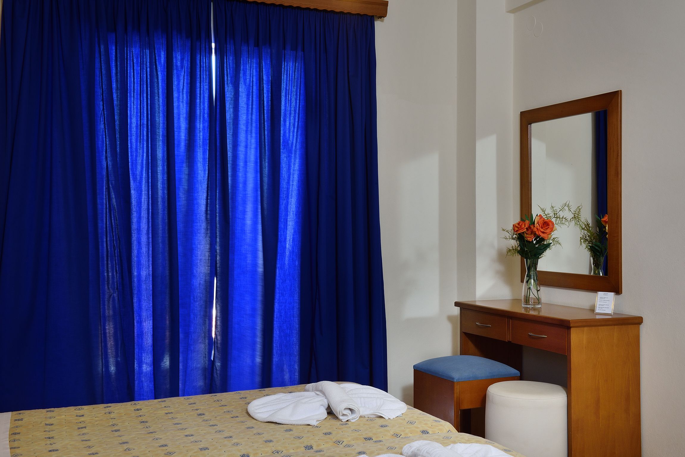 A hotel room with a bed, a wooden dresser, a mirror, and a blue curtain.