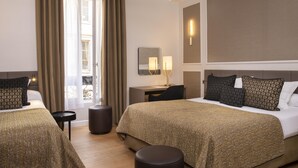 A hotel room with two beds, a desk, a chair, a small table, and a window with curtains. - Hôtel du Levant (Paris)