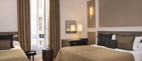 A hotel room with two beds, a desk, a chair, a small table, and a window with curtains.
