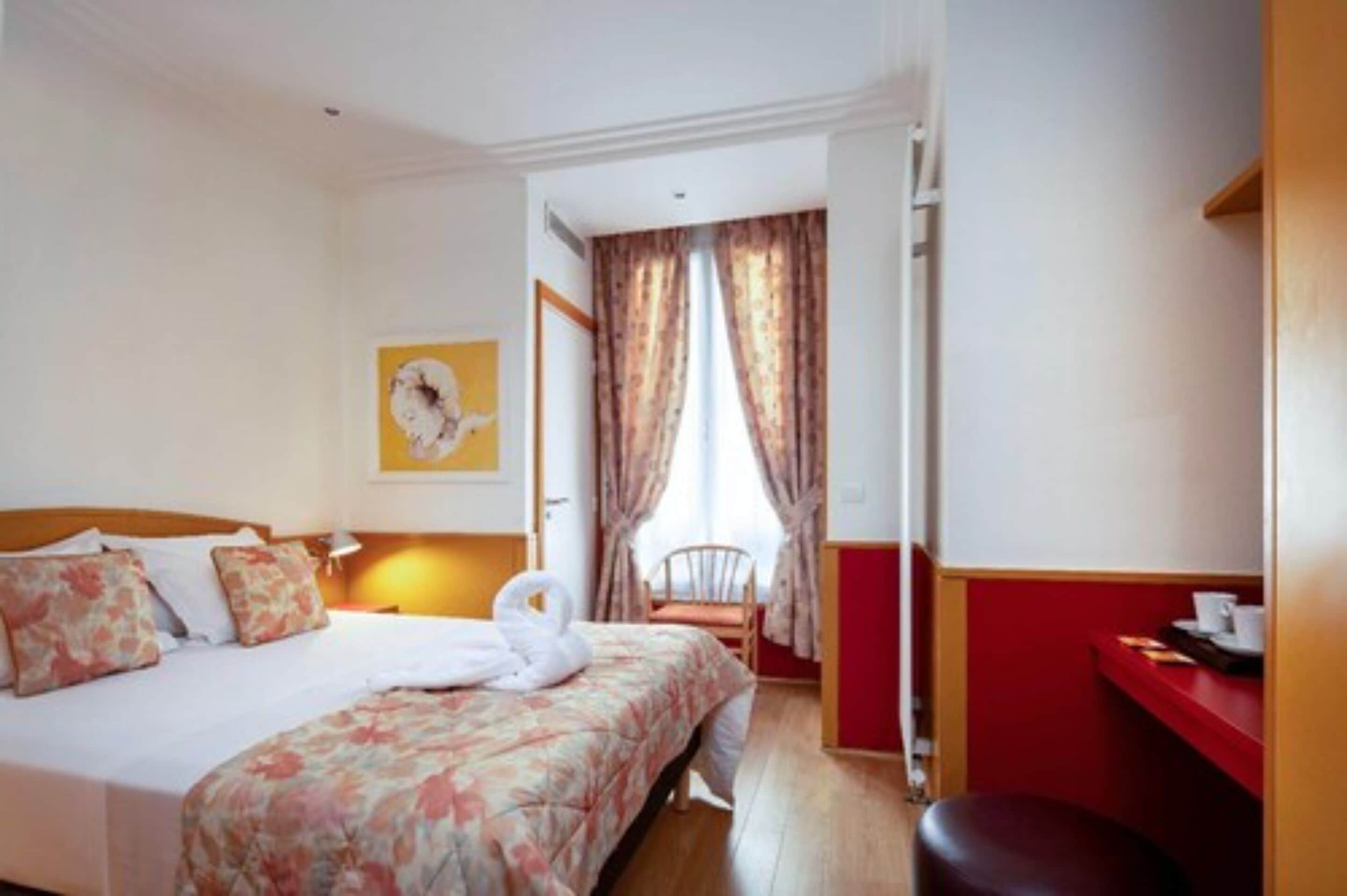 A hotel room with a bed, a chair, a desk, and a window with curtains.