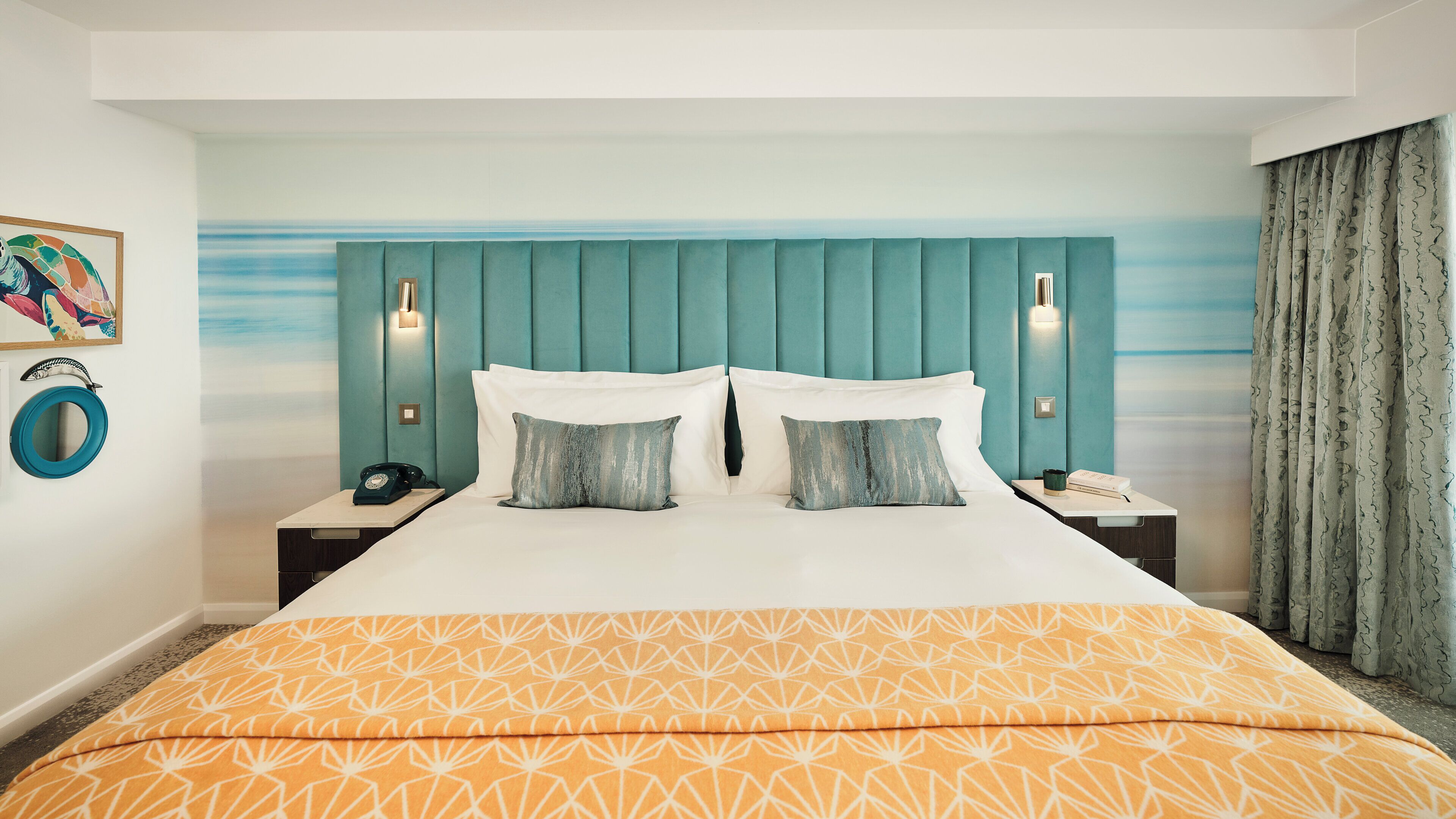 A hotel room with a bed, two bedside tables, a nightstand, a wall-mounted telephone, and a painting.