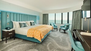 Habitación de hotel con una cama grande, un escritorio, una silla y vista al océano.