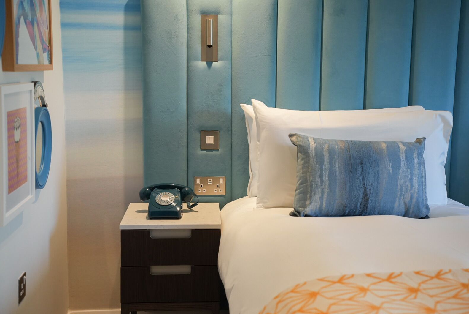 Une chambre à coucher avec un lit, une table de chevet sur laquelle se trouve un téléphone à cadran, et un interrupteur fixé au mur.