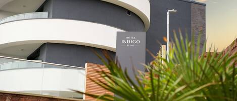 A modern hotel with a curved facade, a sign reading "HOTEL INDIGO BY IHG," and a view of the sky.
