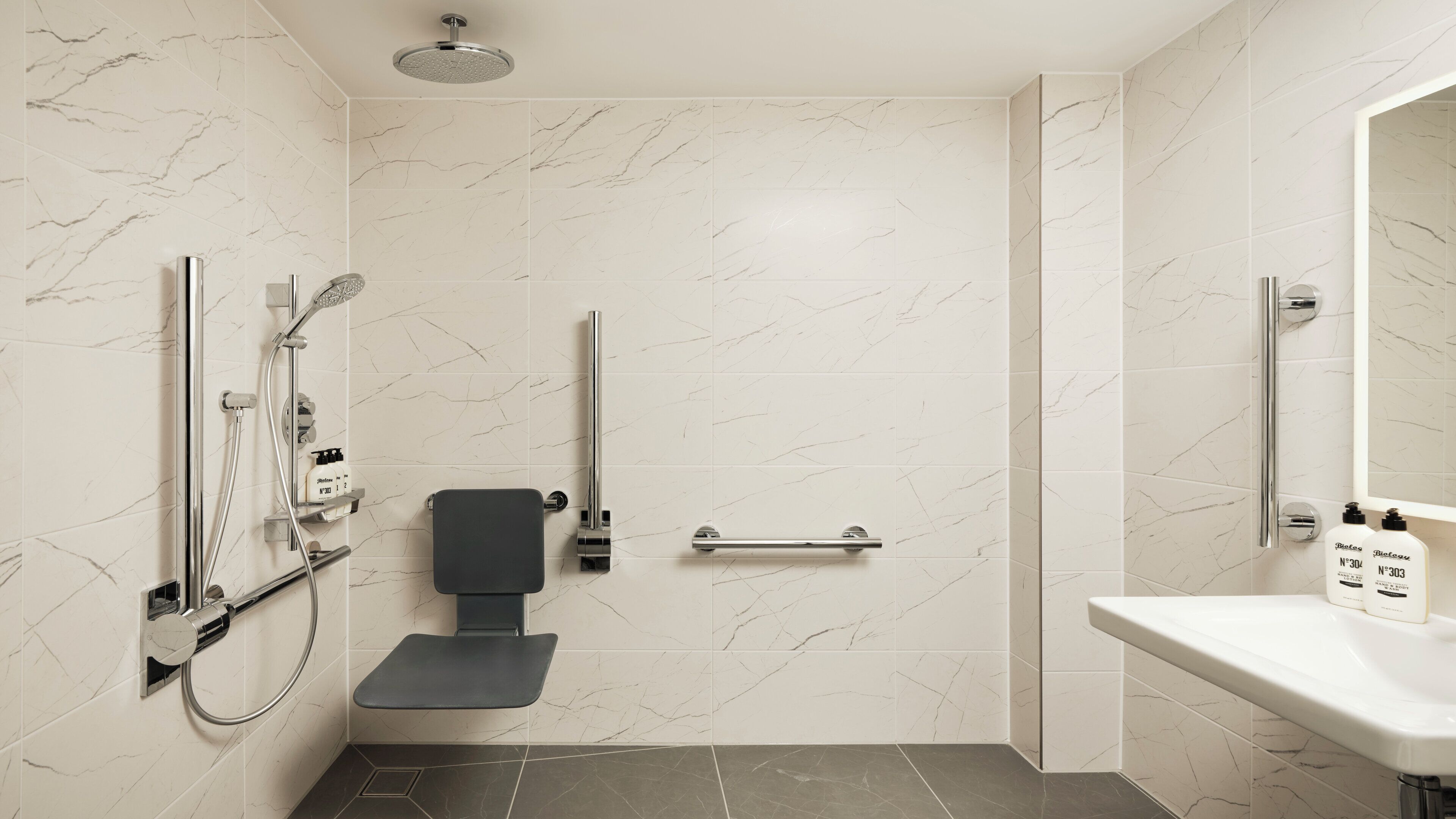 A modern bathroom with a walk-in shower, a toilet with a grab bar, and a sink with hand soap.
