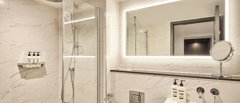 A modern bathroom with a glass-enclosed shower, a vanity with a mirror, and toiletries on the sink.