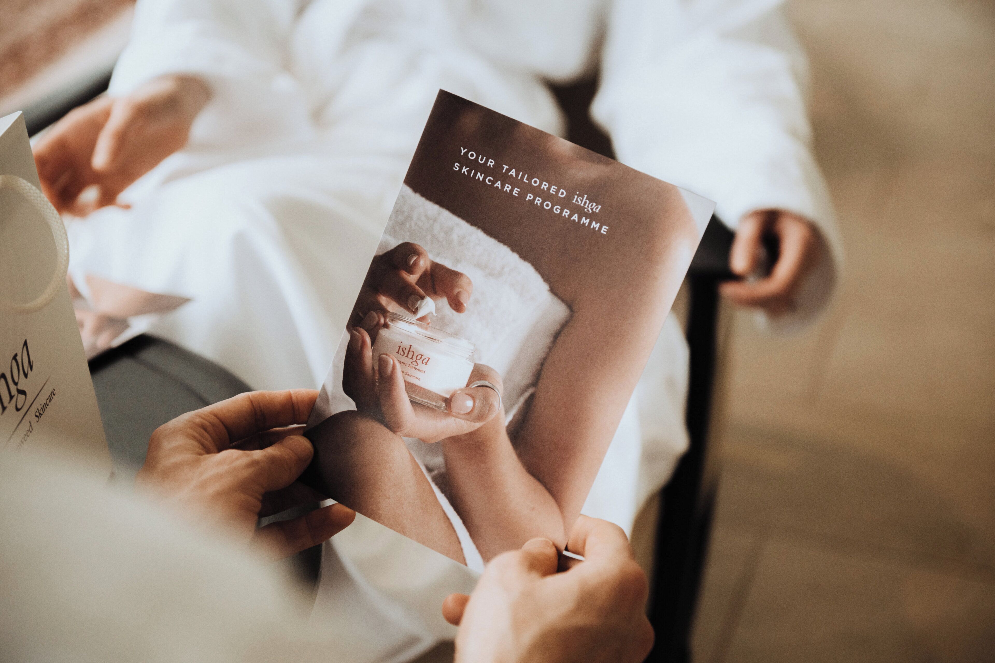 A person holding a brochure with the text 'YOUR TAILORED ishga SKINCARE PROGRAMME' and a picture of a hand applying a product.
