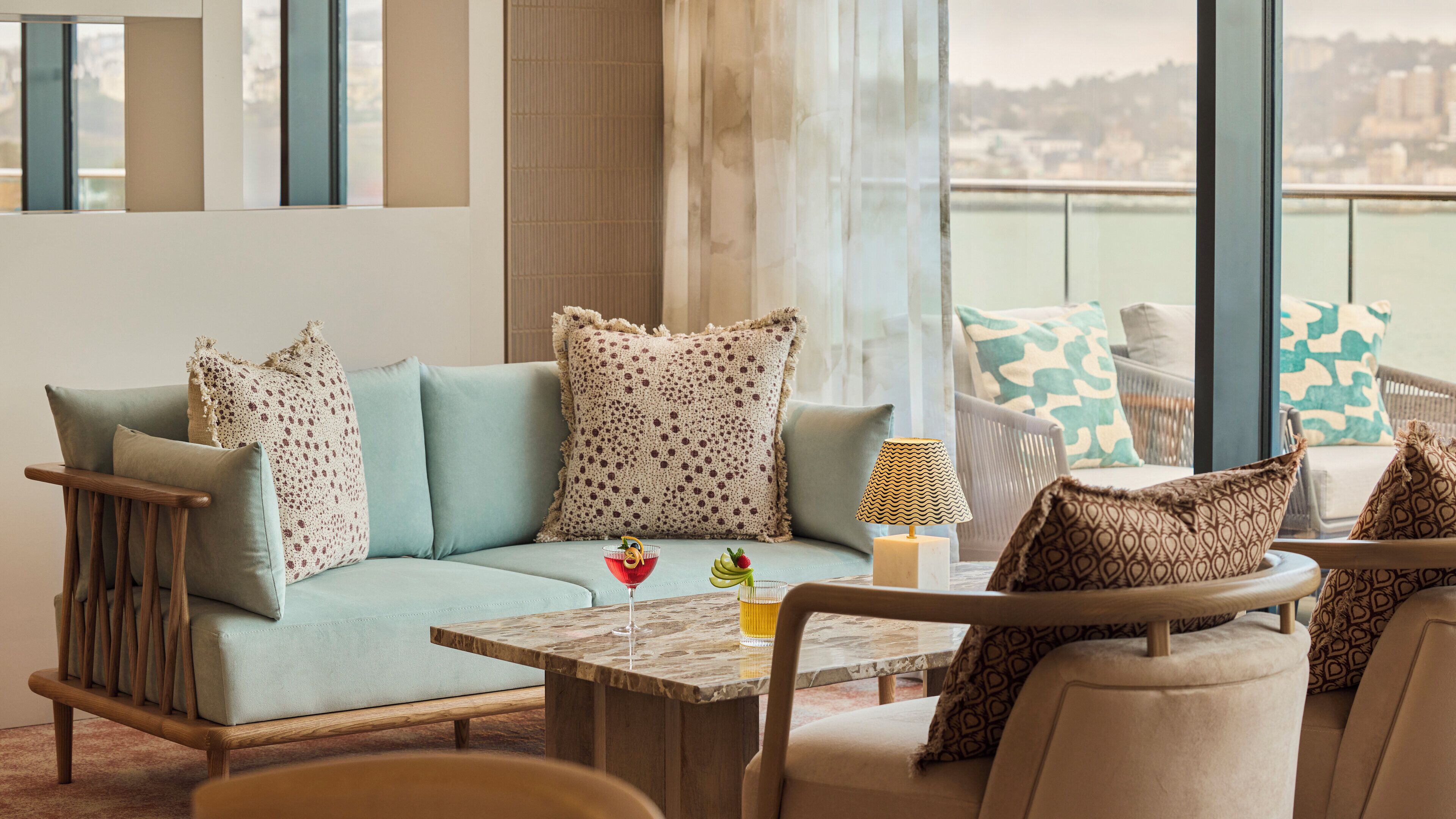 A modern lounge area with a sofa, chairs, a table, and a view of the city.