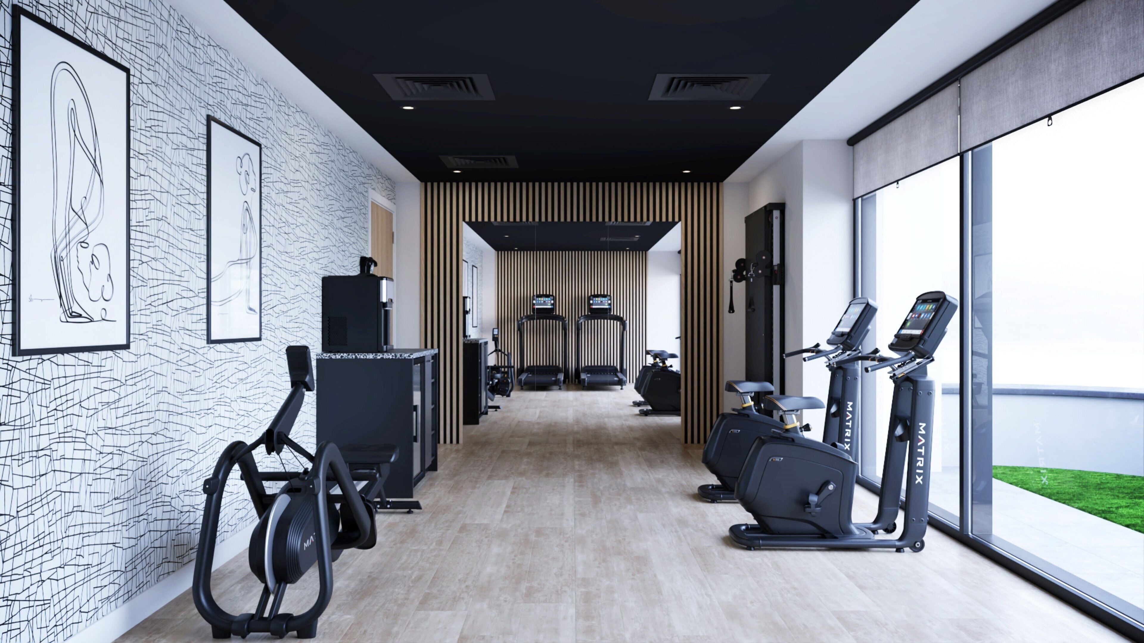 Un gimnasio moderno con equipo de cardio, un televisor montado en la pared y grandes ventanales con vistas al exterior.