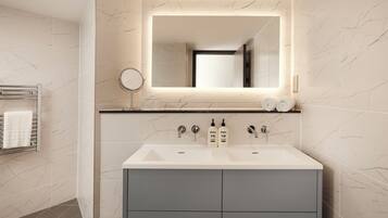 A modern bathroom with a double sink, a mirror, and two bottles of shampoo.
