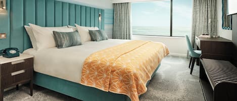 Habitación de hotel con una cama grande, un escritorio y vistas al océano.