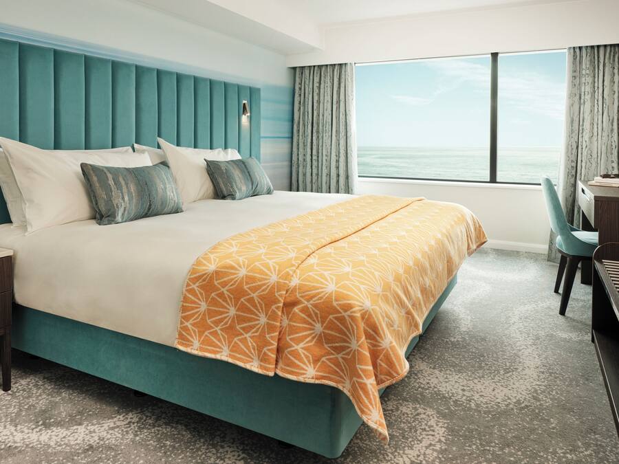 A hotel room with a large bed, a desk, and a view of the ocean.