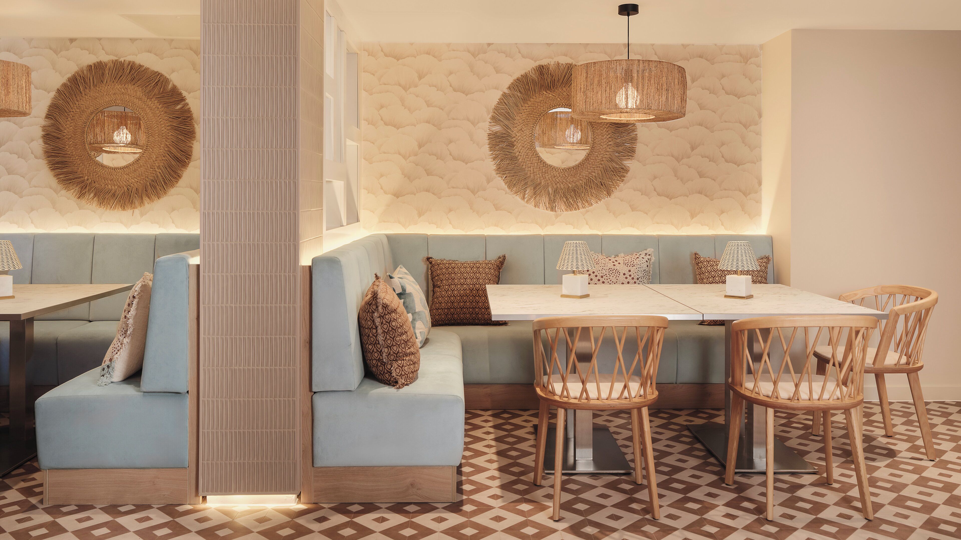A modern restaurant interior with a central seating area, wooden chairs, and a patterned floor.