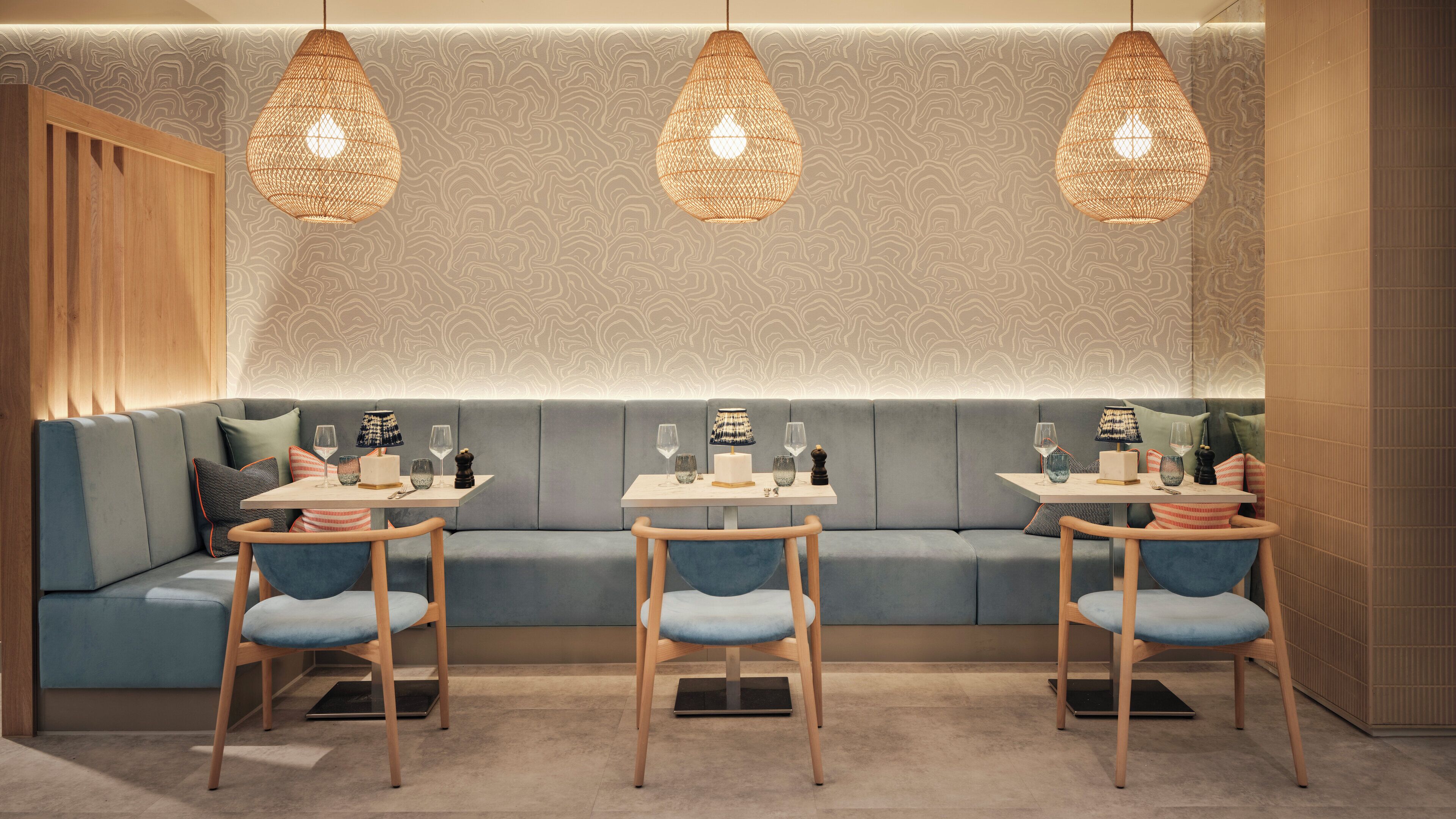 A modern dining area with a long bench, three tables, and hanging wicker lamps.