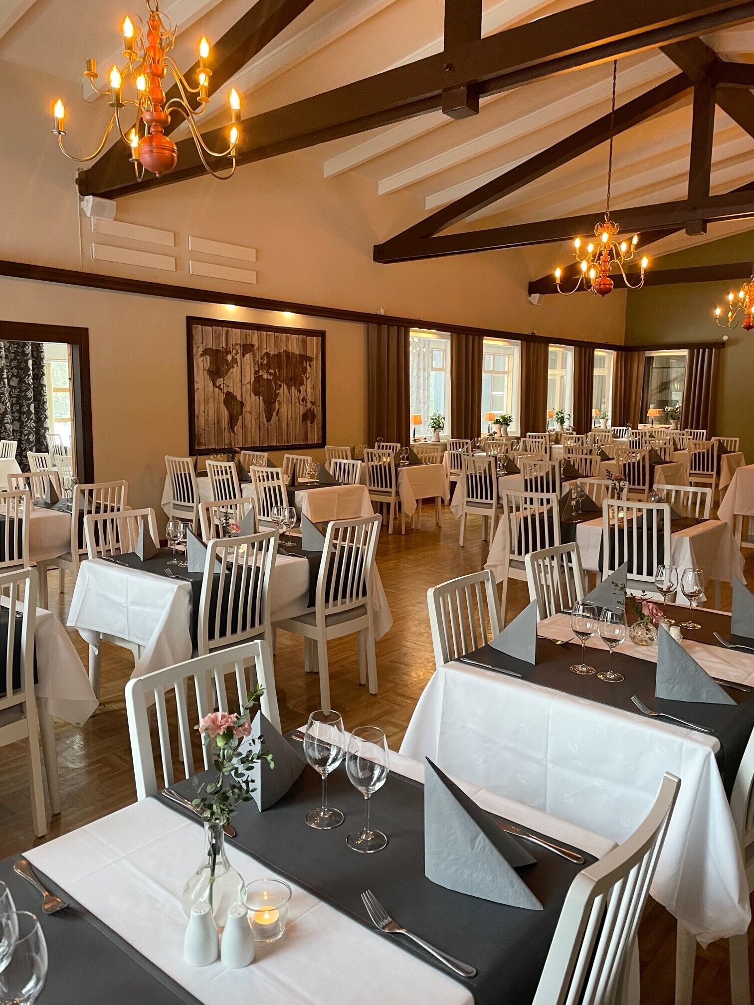A restaurant with multiple tables set for dining, white chairs, and chandeliers.