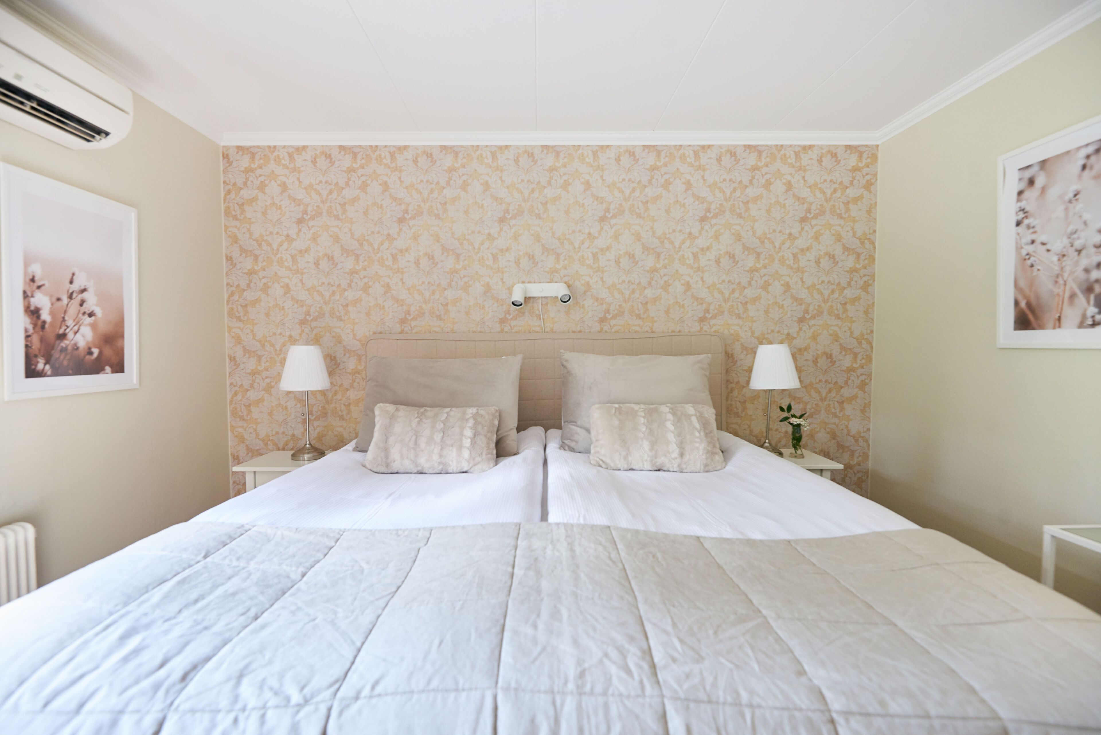 A double bed with a quilted white bedspread, two bedside tables with lamps, and a wall-mounted light fixture.