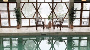 A pool area with two wicker chairs and potted plants, large windows with a view of trees, and a tiled floor. - Mullsjö Hotell och konferens (Mullsjö)