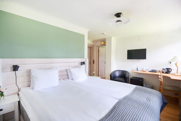 A hotel room with a large bed, a desk with a chair, a television, and a small refrigerator.