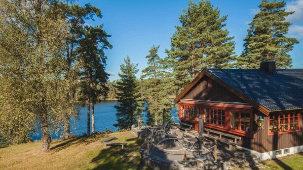 A cabin by a lake with a stone patio, wooden deck, and a red exterior. - Mullsjö Hotell och konferens (Mullsjö)
