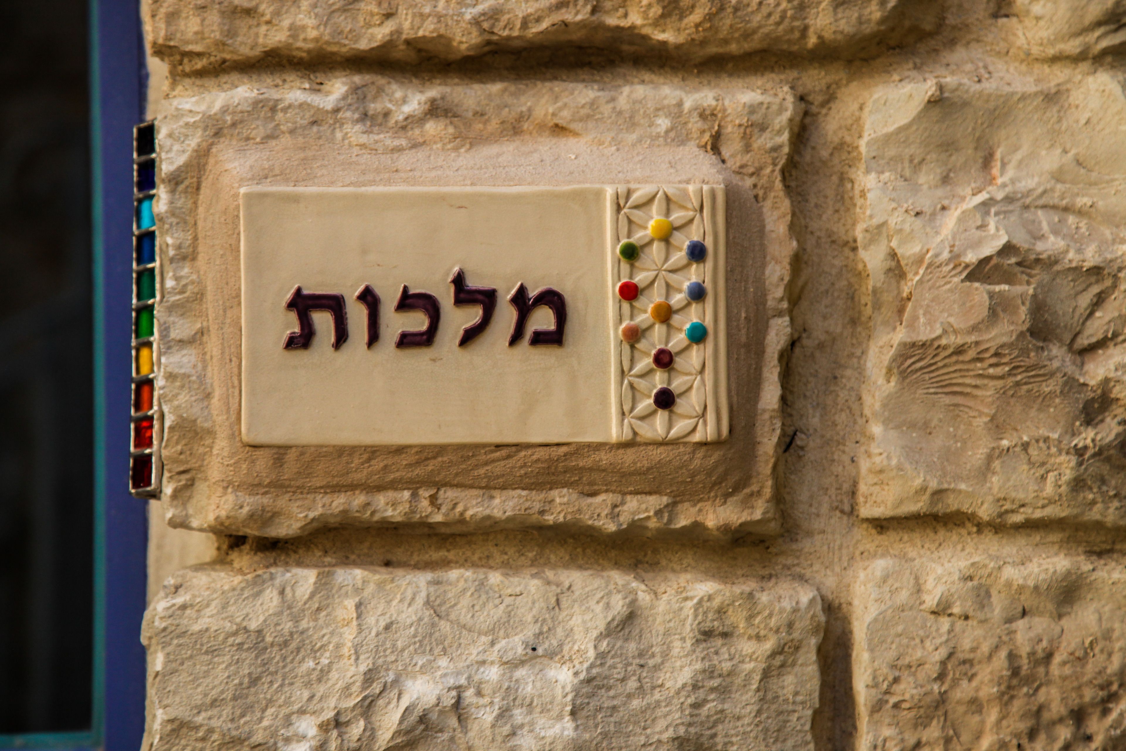 A stone wall with a beige plaque featuring Hebrew text and colorful dots.