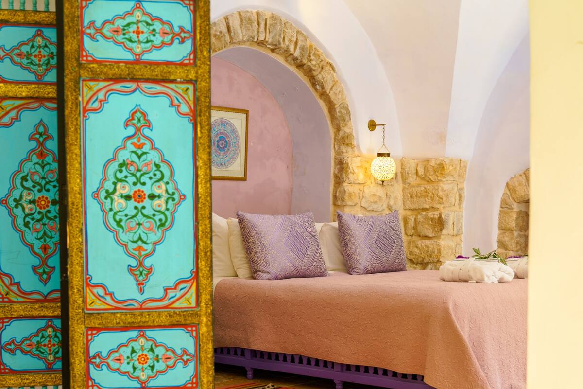 A bedroom with a stone archway, a bed with patterned pillows, and a decorative wall panel.