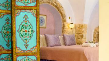 A bedroom with a stone archway, a bed with patterned pillows, and a decorative wall panel.