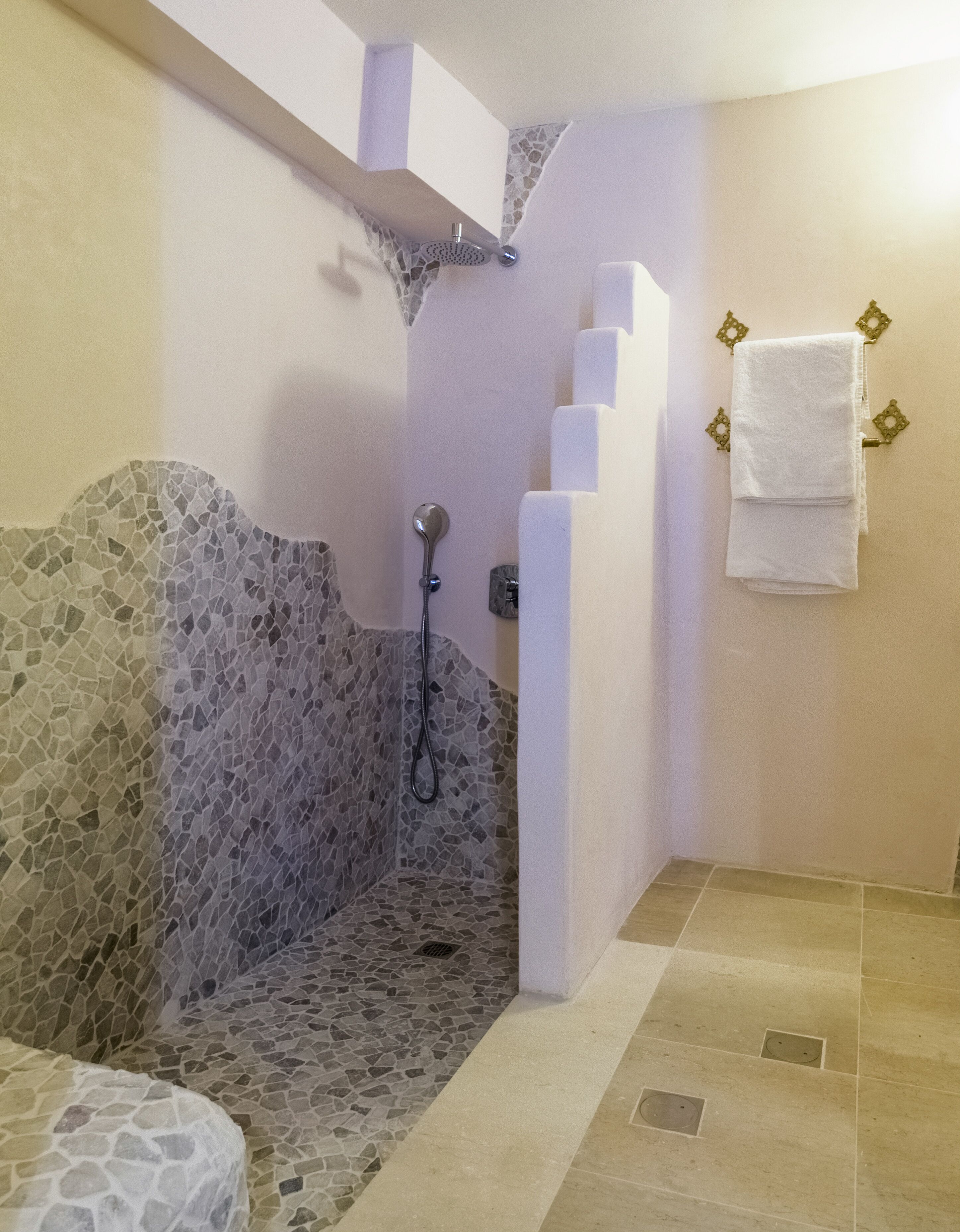 A bathroom with a stone shower enclosure, a white towel rack, and tiled flooring.