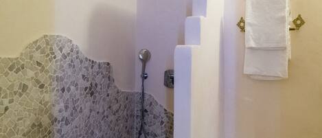 A bathroom with a stone shower enclosure, a white towel rack, and tiled flooring.
