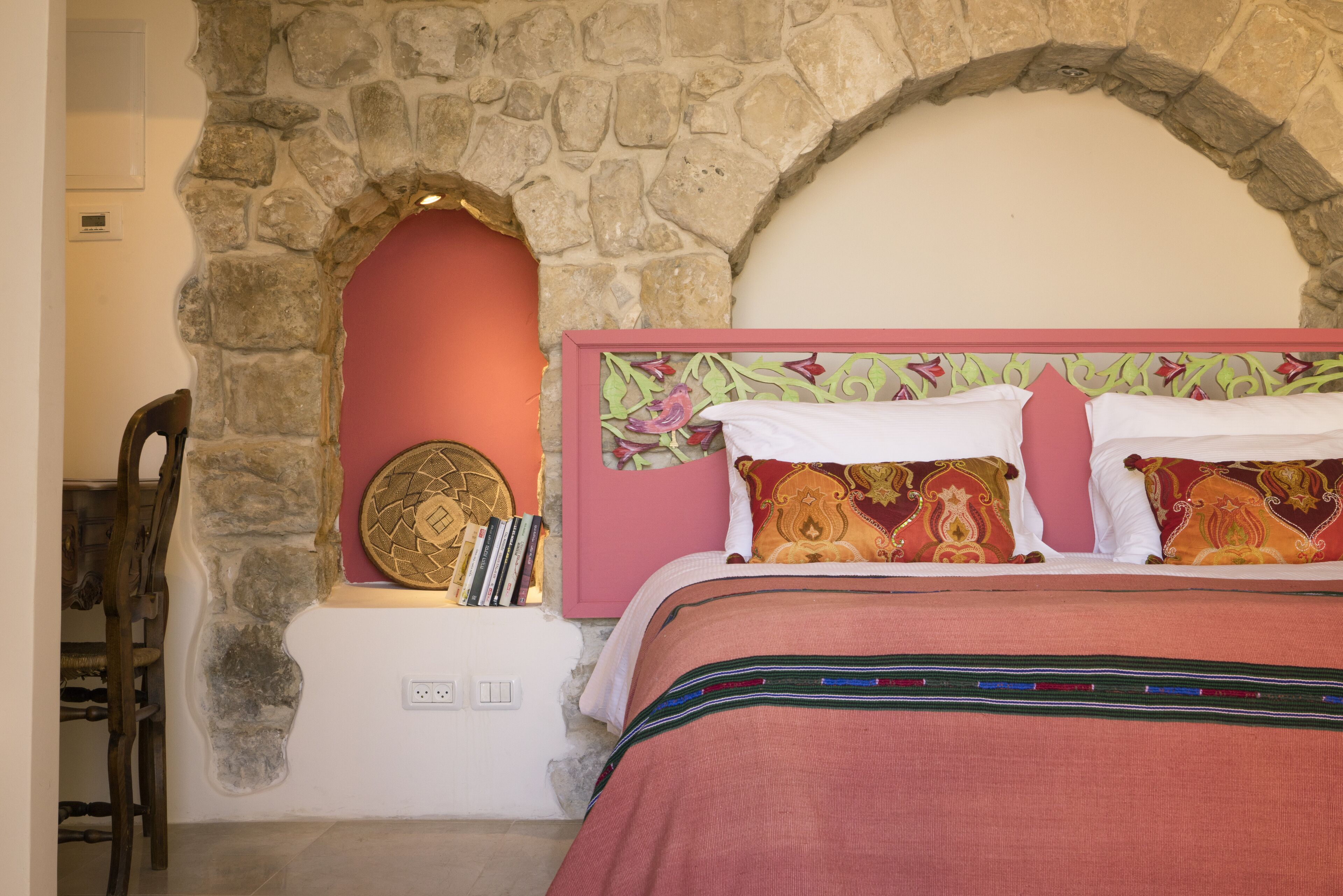 A bedroom with a stone archway, a bed with patterned pillows, and a decorative headboard.