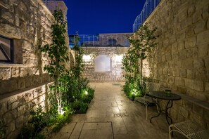 A stone courtyard with a small table and chairs, surrounded by greenery and illuminated by soft lighting. - The Way Inn (Safed)