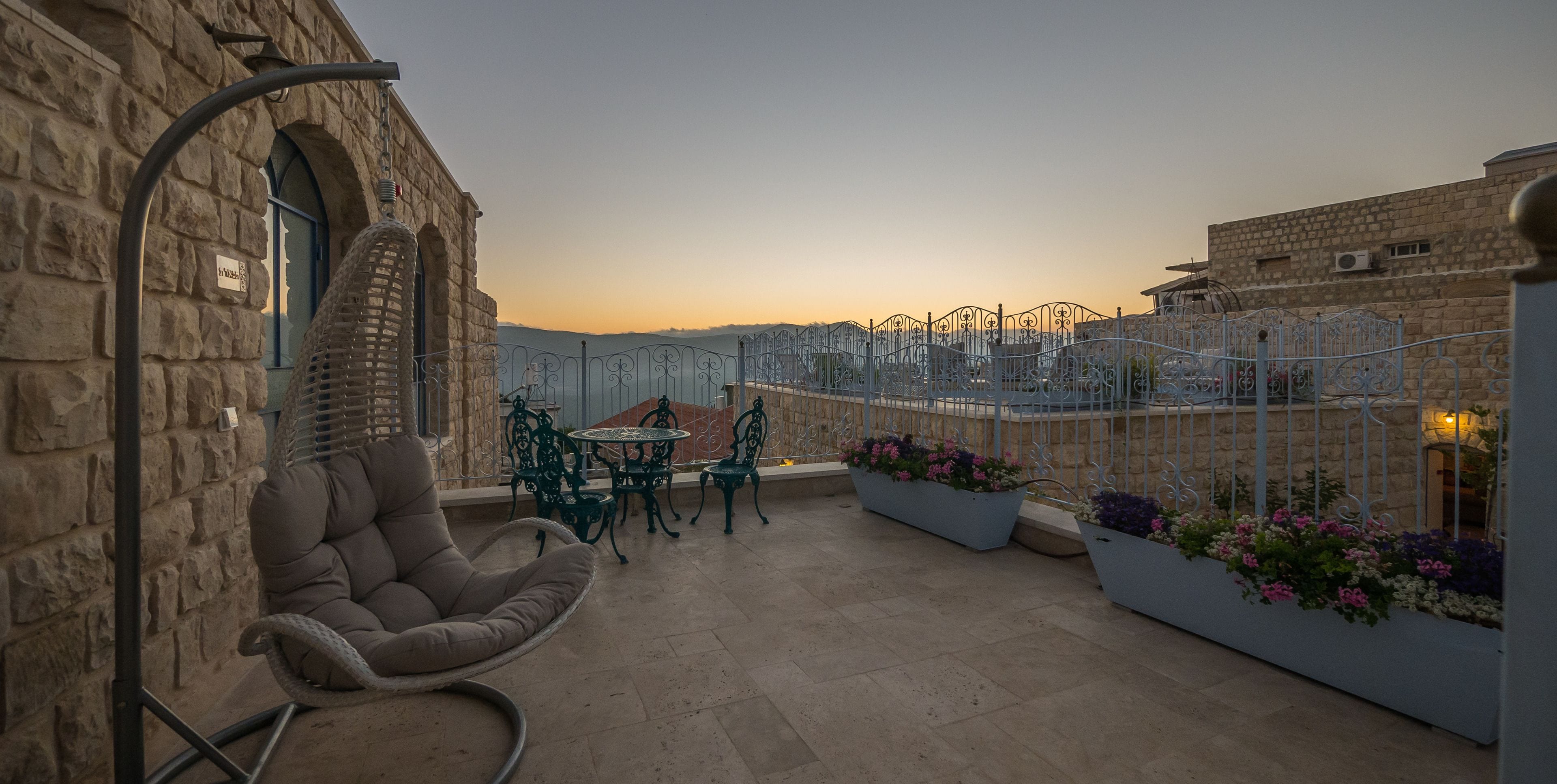 Una terraza con muros de piedra, una silla acolchada, una mesa redonda y sillas de metal.