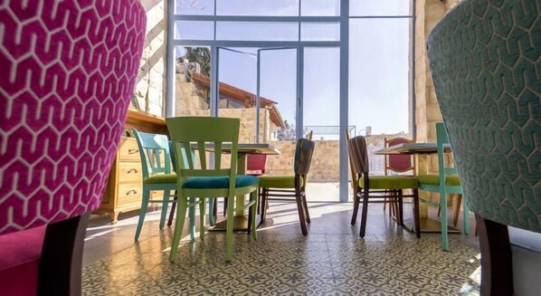A room with a large window, green chairs, and a patterned floor. - The Way Inn (Safed)