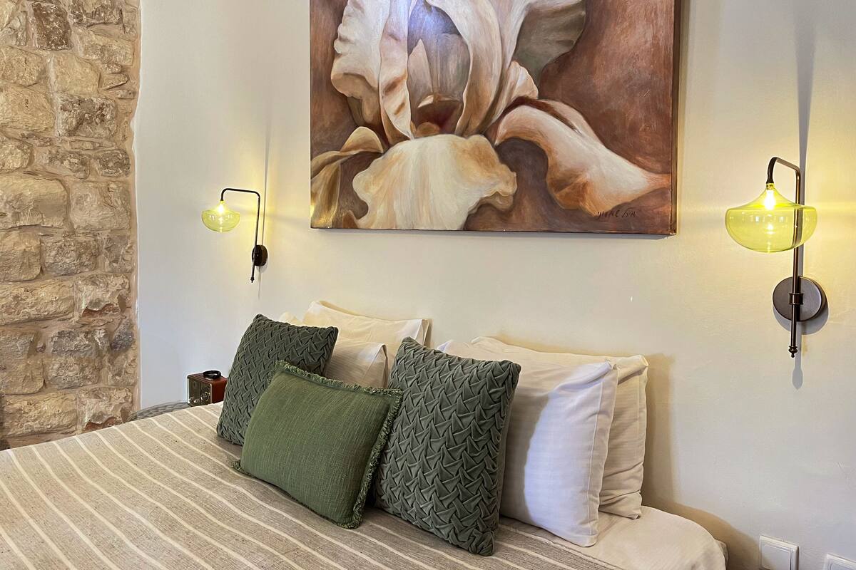 A bedroom with a stone wall, a bed with striped bedding, green and white pillows, and a large floral painting.