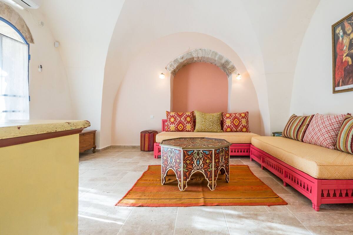 A cozy living room with a pink sofa, a patterned coffee table, and a colorful rug.