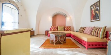 Una sala de estar acogedora con un sofá rosa, una mesa de centro estampada y una alfombra colorida.