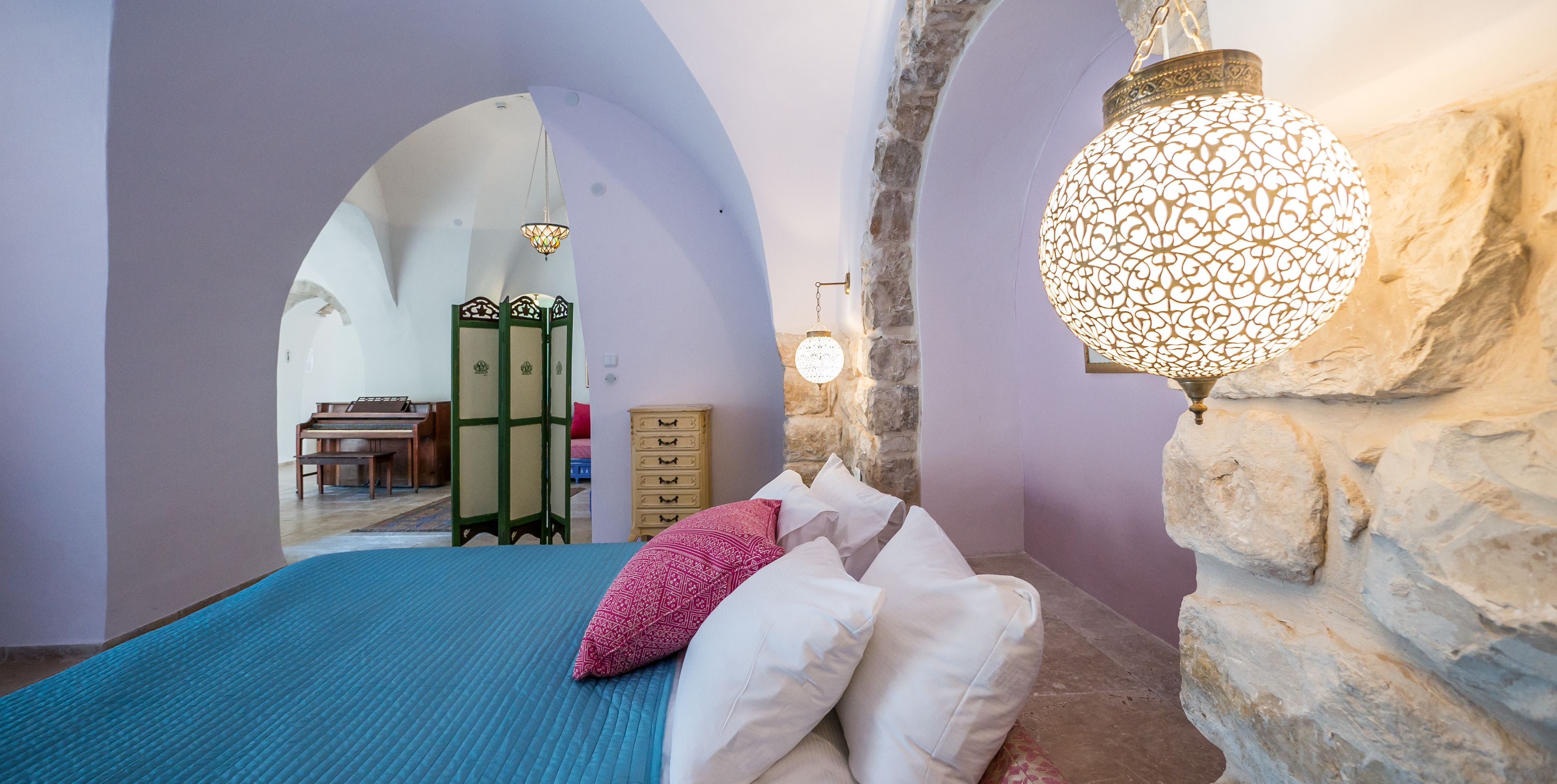 A bedroom with a bed, pillows, a stone wall, and a hanging light fixture.