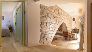 Habitació amb arc de pedra a la paret que condueix a una zona de menjador amb mobiliari de fusta i una catifes amb dibuixos.