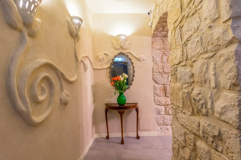 A hallway with a stone wall, a wooden table with a vase of flowers, and a mirror on the wall.