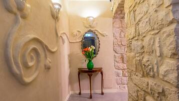 A hallway with a stone wall, a wooden table with a vase of flowers, and a mirror on the wall.