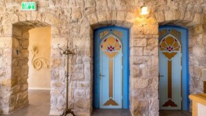 Passadís de pedra amb dues portes blaves, una amb un dibuix decoratiu i una lluminària a sobre.