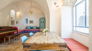 A room with a wooden table, blue chairs, a piano, and a cozy seating area with cushions.