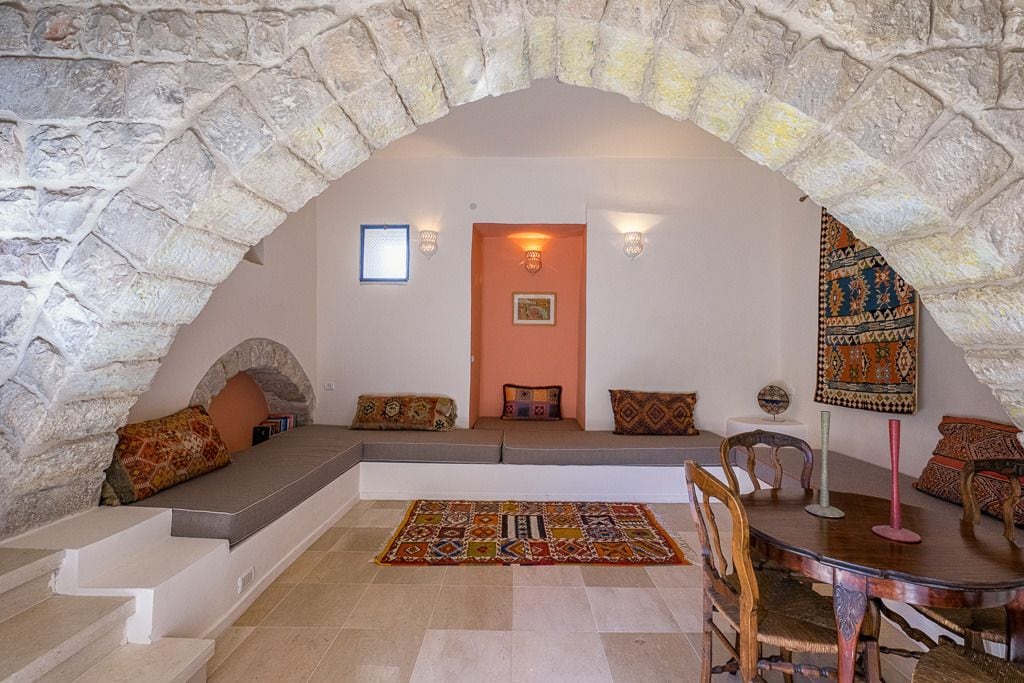 Una habitación acogedora con un arco de piedra, una zona de estar con cojines, una alfombra estampada y una mesa de comedor con sillas.