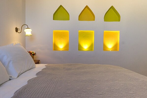 Un dormitorio con cama, una mesita de noche con un florero y lámparas fijadas a la pared.