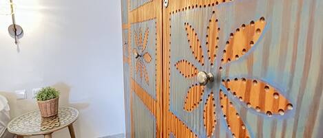 A room with a wooden door featuring a geometric pattern, a small round table with a woven basket, and a wall-mounted light fixture.