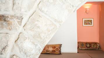 A room with a stone wall, a peach-colored wall, and a framed picture. There are two patterned cushions on a brown sofa.