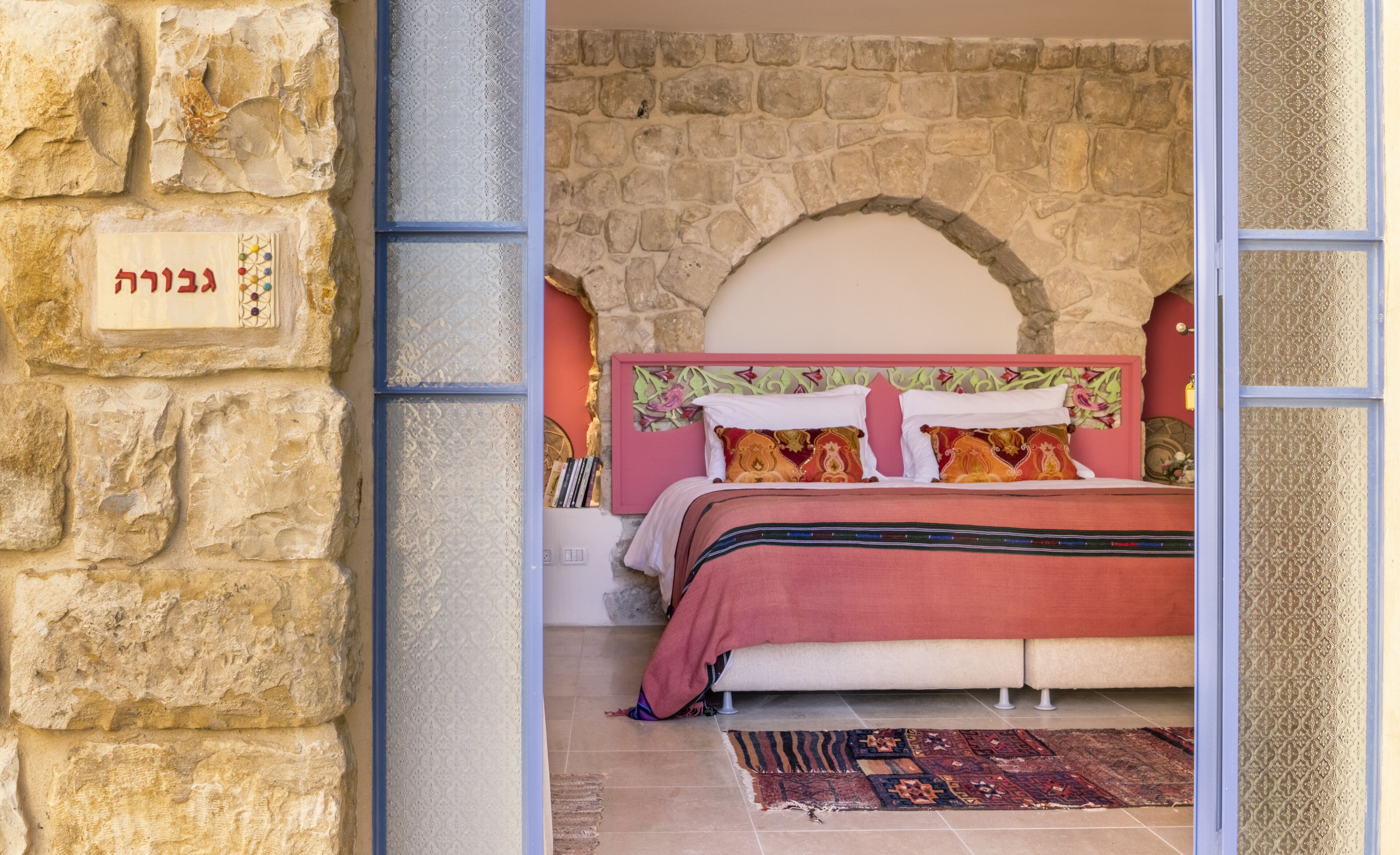 Un dormitorio con pared de piedra, cama con ropa de cama colorida y una pequeña alfombra.
